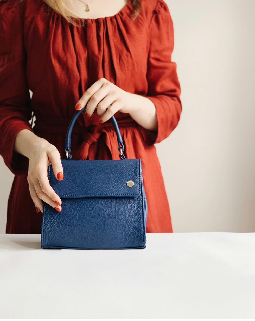 Woman presenting a structured blue leather handbag — graduating from pre-selling to owning her own brand
