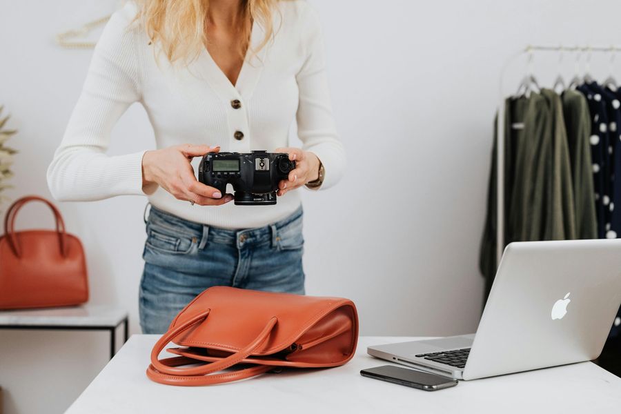 Fashion influencer photographing a terracotta handbag with a camera and laptop on the table