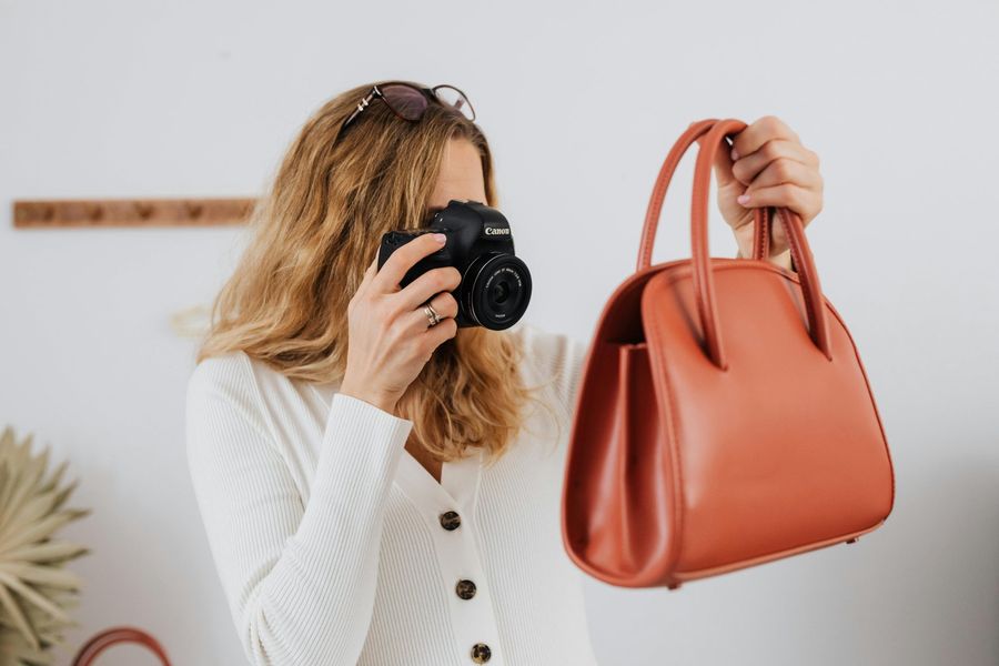 Influencer holding a terracotta handbag while photographing it with a Canon camera