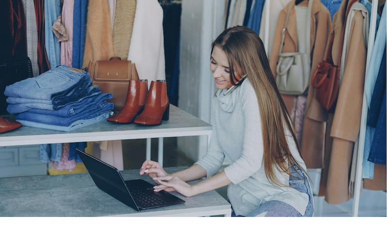 Fashion boutique owner sourcing inventory on laptop while managing calls in her store