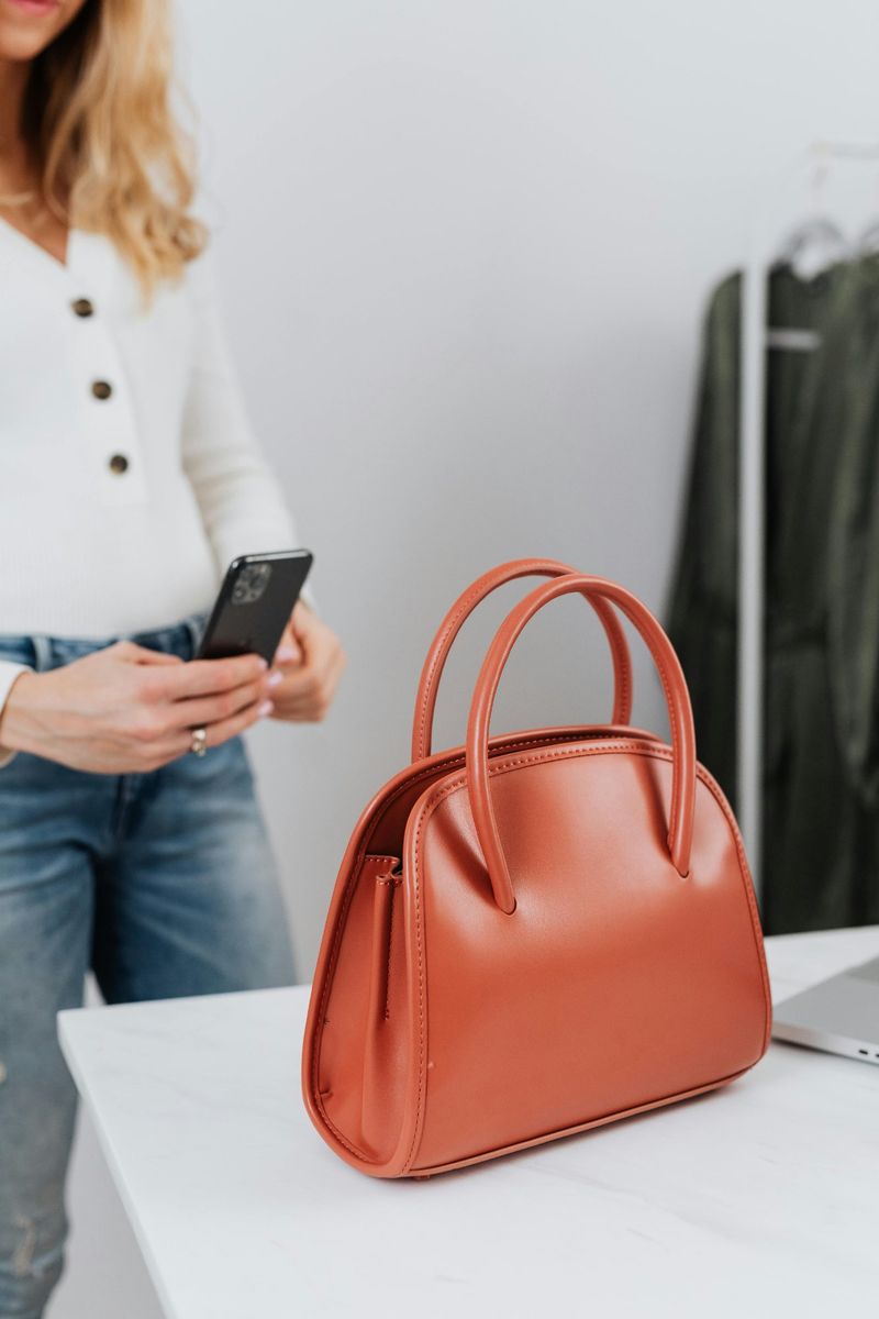 Influencer checking her phone next to a terracotta handbag on a white table